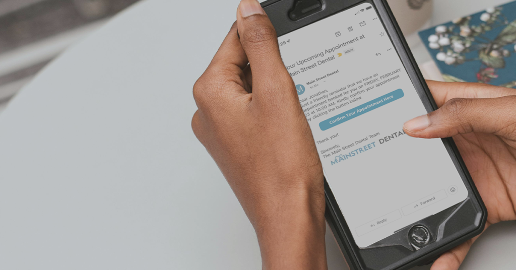 A pair of hands holding a phone looking at an email. The email is an example of an appointment confirmation email sent via ABELDent. There is a blue button in the email to confirm the appointment.
