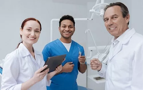 Workflow-System-Navigation Three dental professionals in an operatory room smiling at the camera